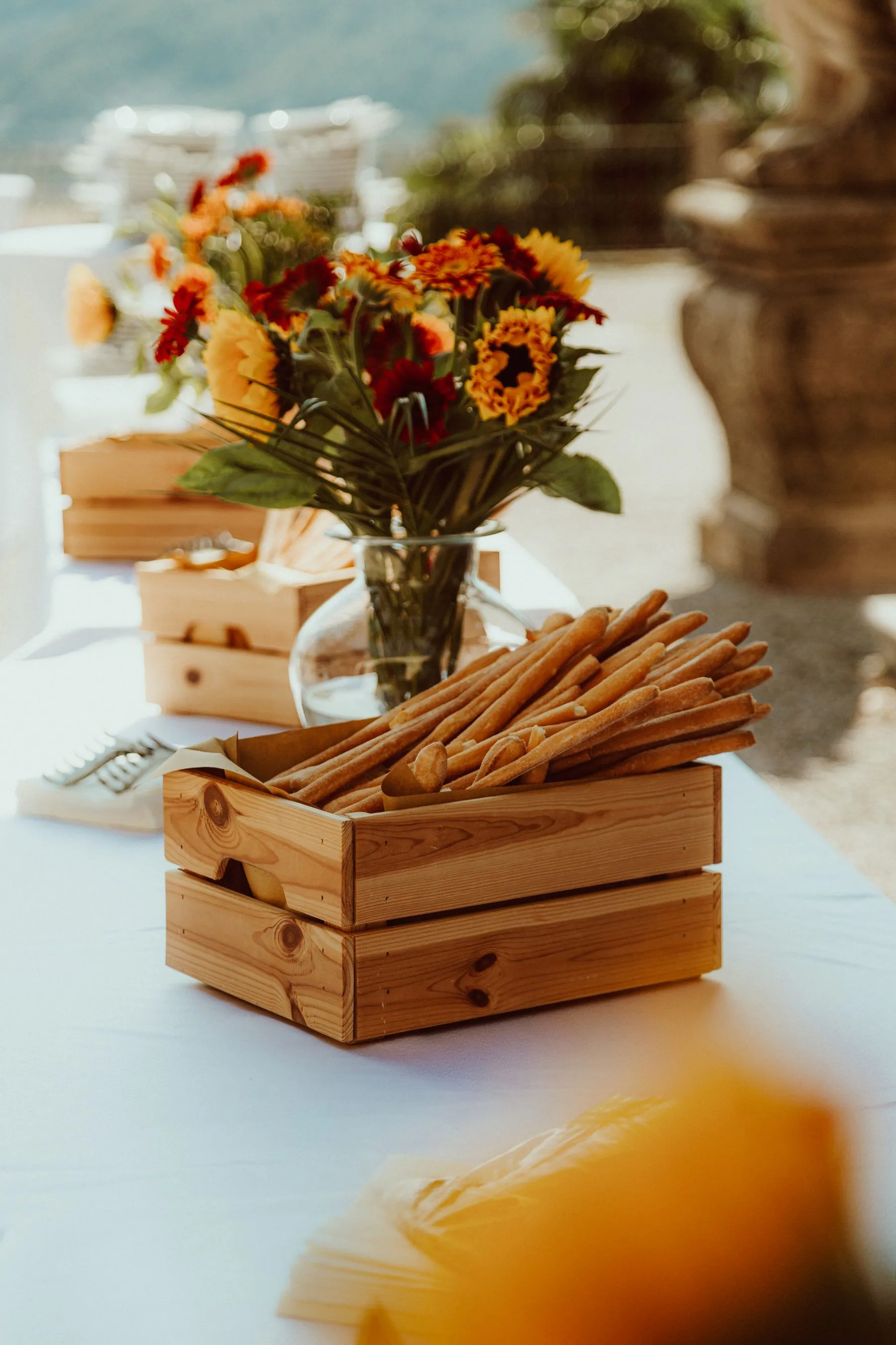 A bouquet beside rustic wooden crates filled with breadsticks at an outdoor reception.